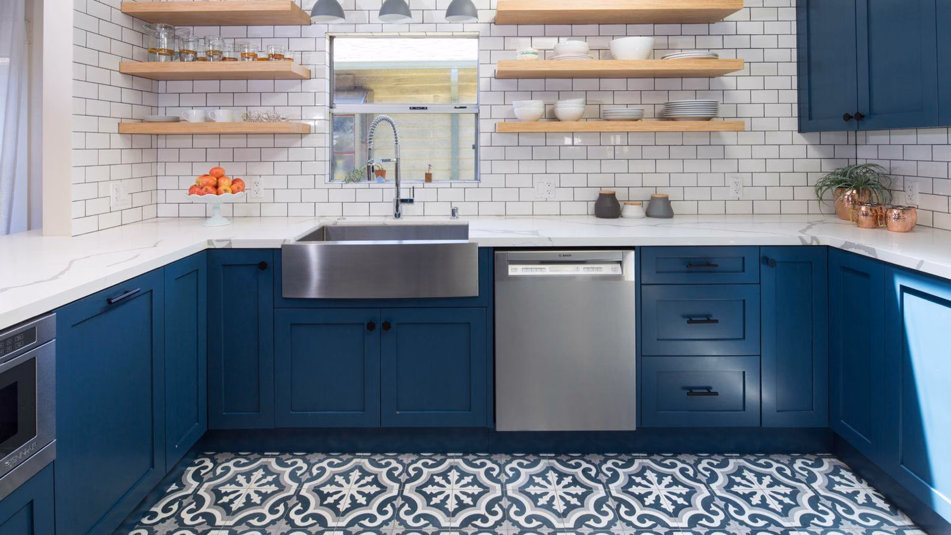 Completed kitchen remodel with navy-blue shaker cabinets, white subway tile, open wood shelving, a stainless farmhouse sink, and patterned encaustic floor tile